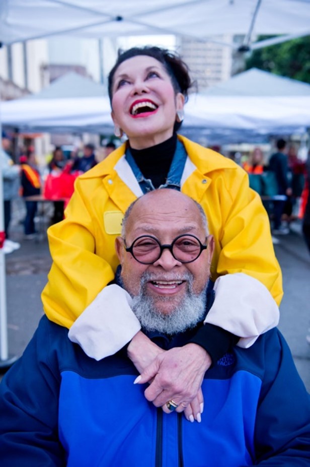Photo of Janice Mirikitani and Cecil Williams laughing together at Grocery Bag Giveaway 2016.